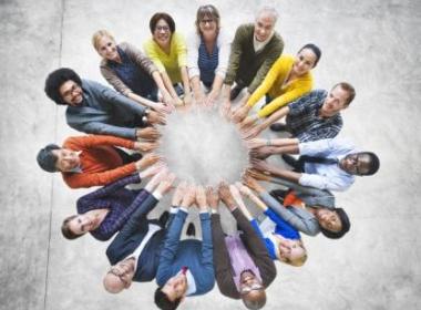 many people of many ethnicities in a circle, holding hands and looking up